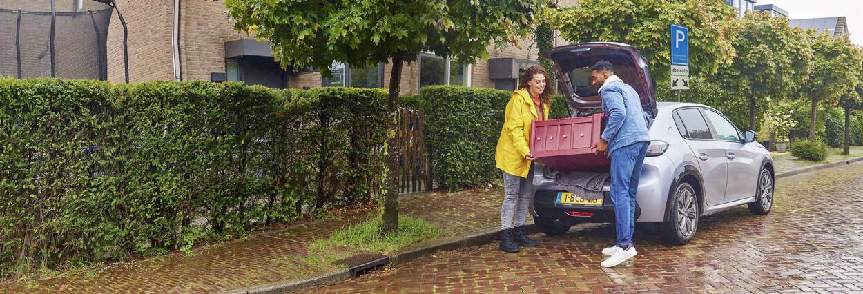 Een man en een vrouw dragen samen een kastje uit een auto