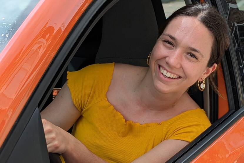 Een jonge vrouw zit achter het stuur van haar auto en hangt haar gezicht uit het raam